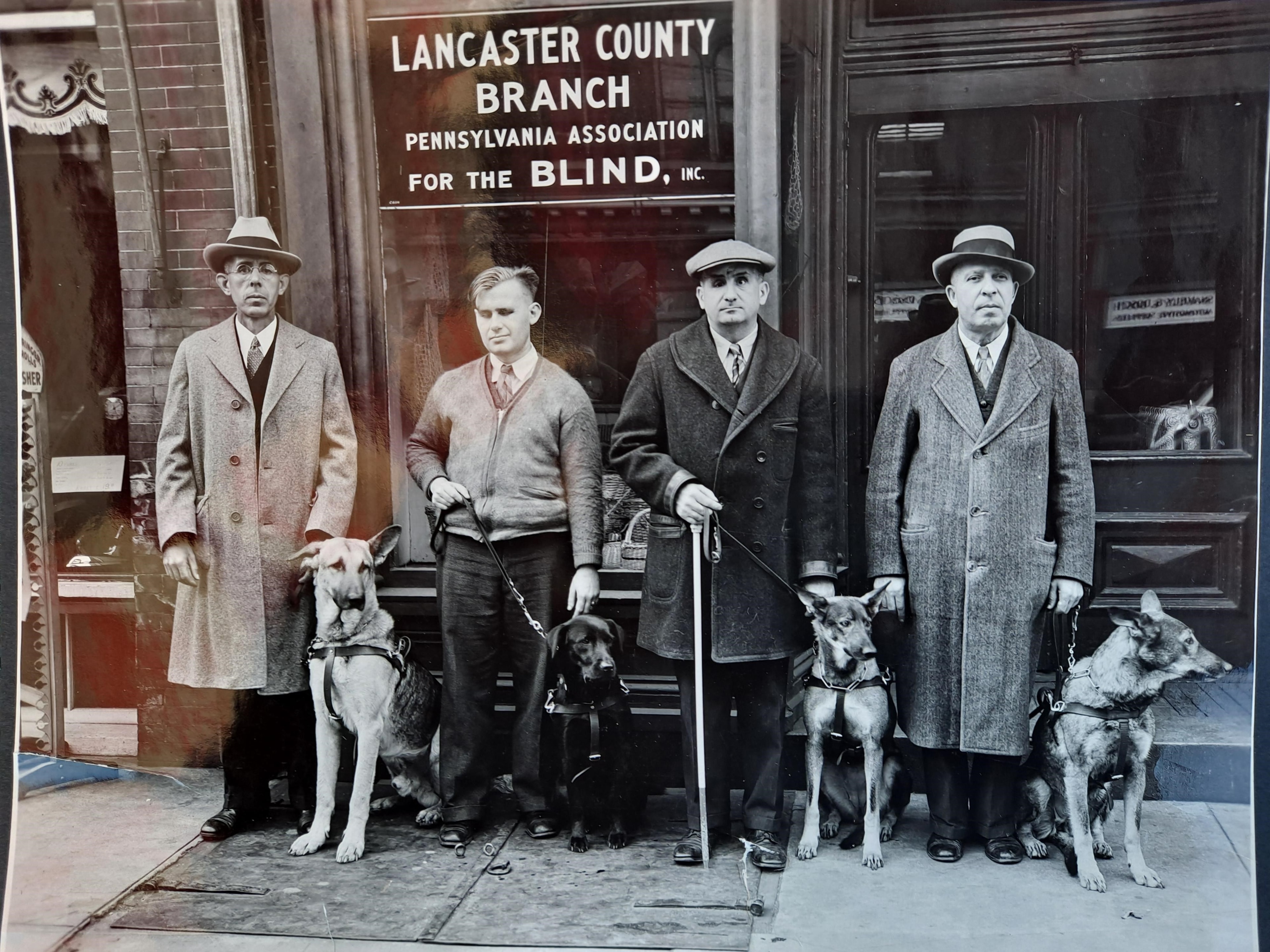 Four men with guide dogs outside the Lancaster County Branch of the Pennsylvania Association for the Blind